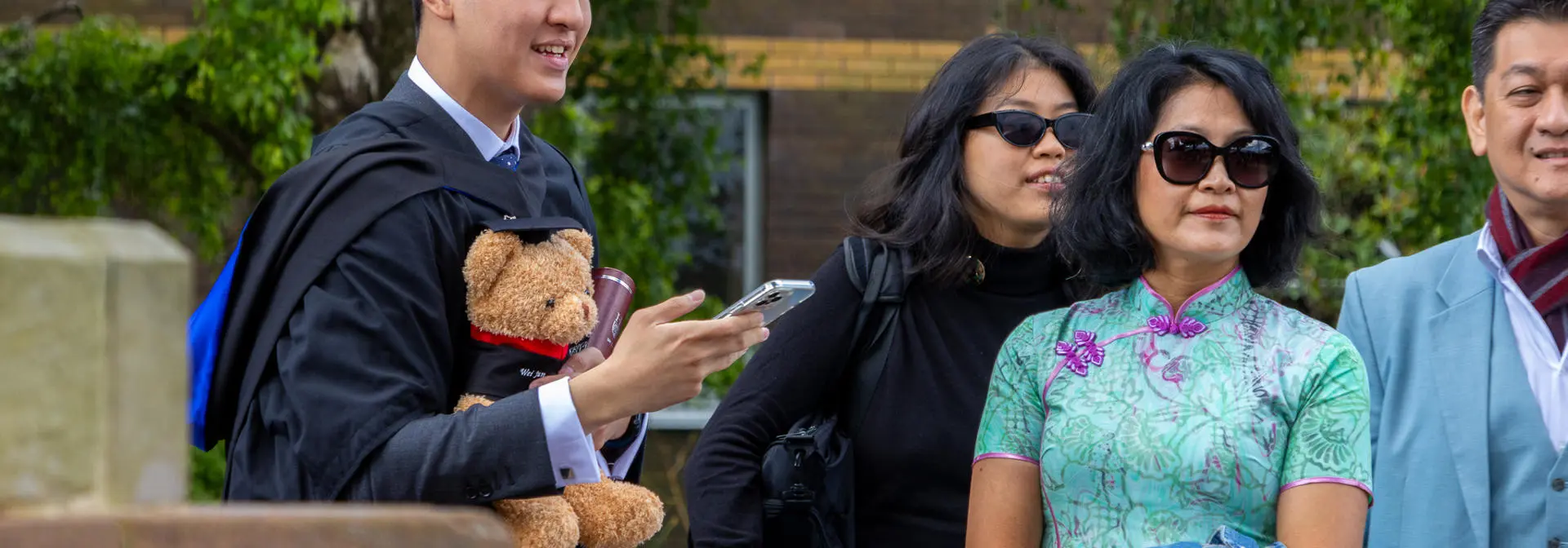 A student holding Heriot-Watt bear with family on graduation day.
