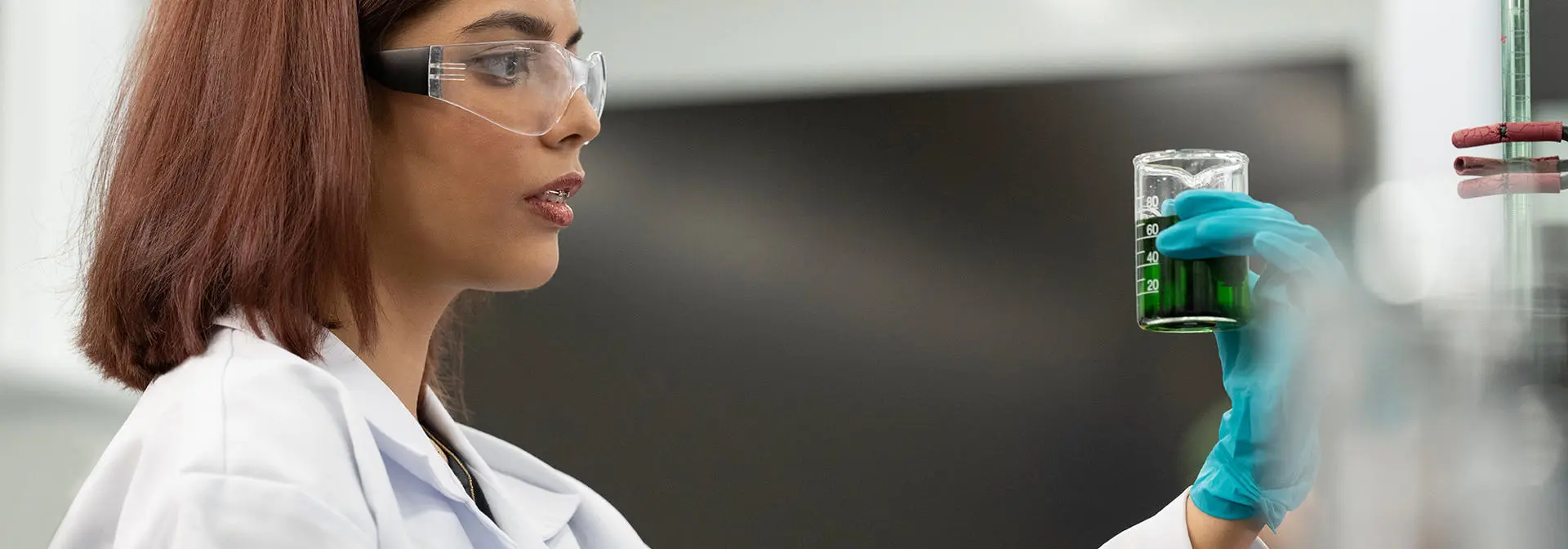 A student wearing safety glasses holds a beaker in a chemistry lab.