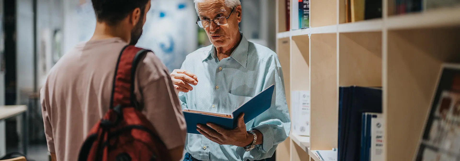 A coach talks through notebook guidance in the library to a student.