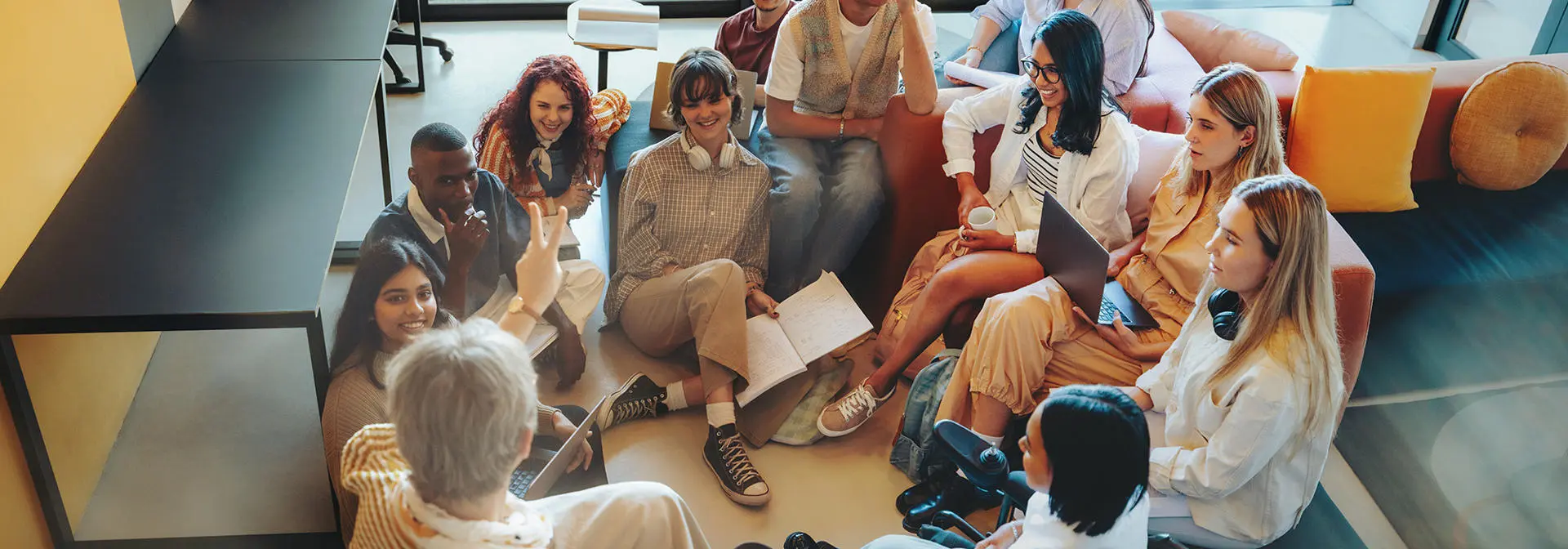 Group of students sitting in a circle on the floor and on chairs in discussion.