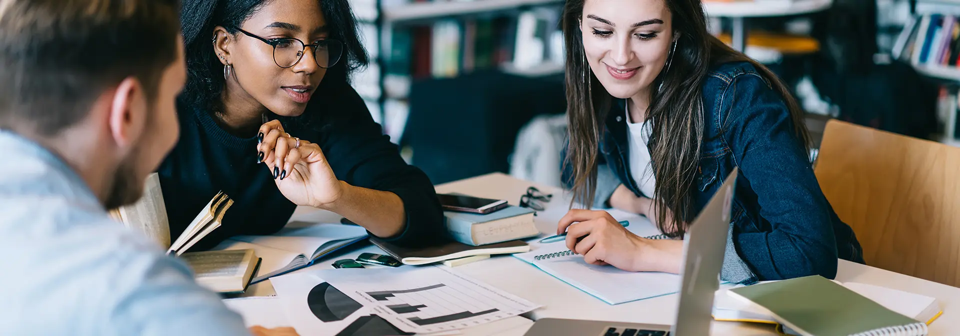 Three students looking at a laptop together while studying in a library.