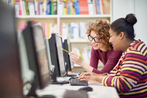 Two individuals working at a computer in a library.