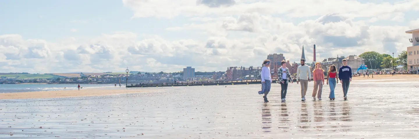 Five individuals walking on wet sand of a beach with the town in the background.