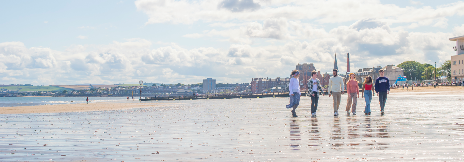 Five individuals walking on wet sand of a beach with the town in the background.