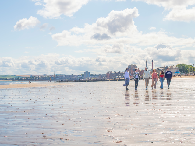 Five individuals walking on wet sand of a beach with the town in the background.