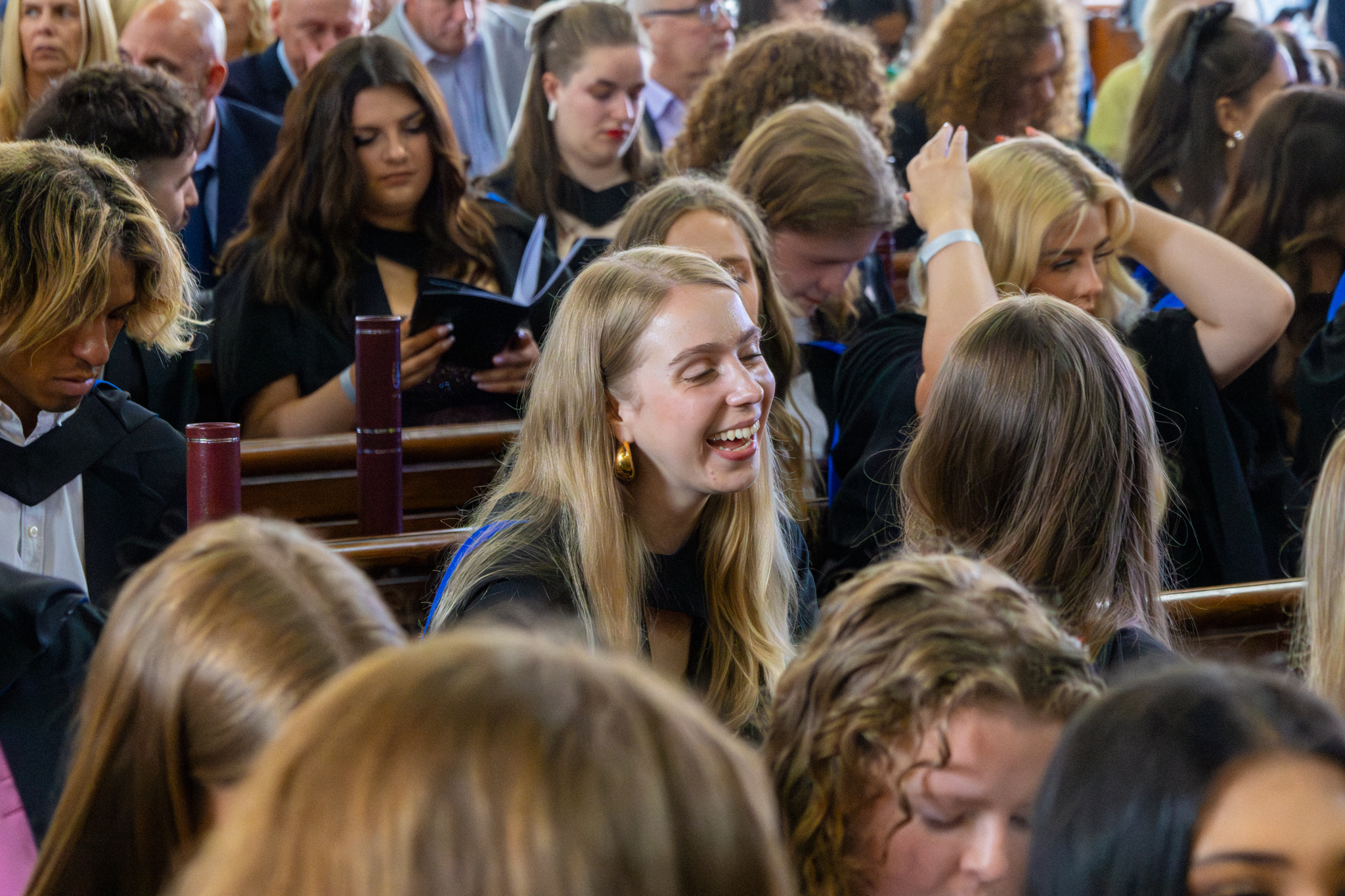 Students laughing in discussion as they sit in the graduation ceremony hall. 