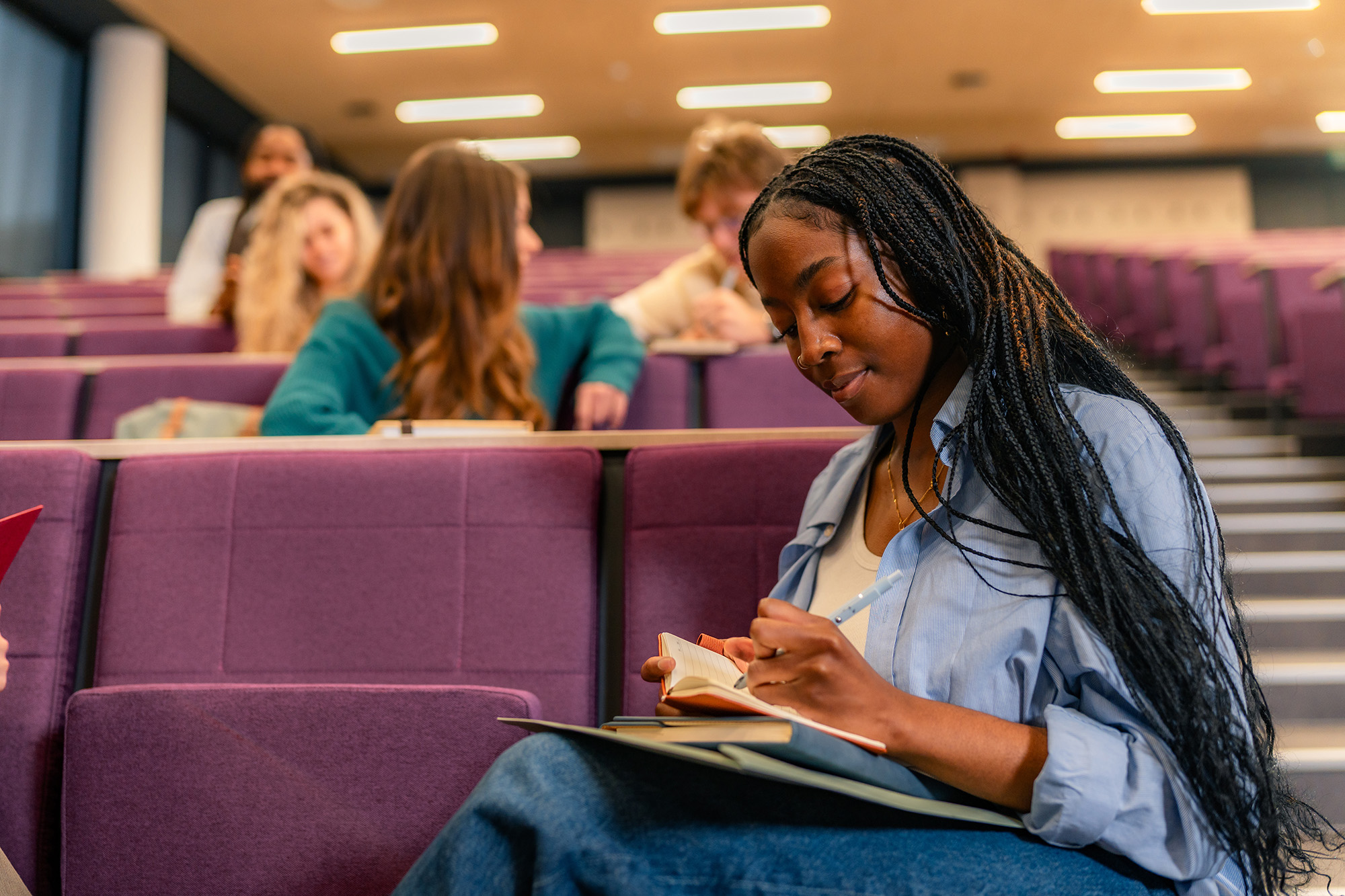 A student takes notes while sitting in a lecture hall.