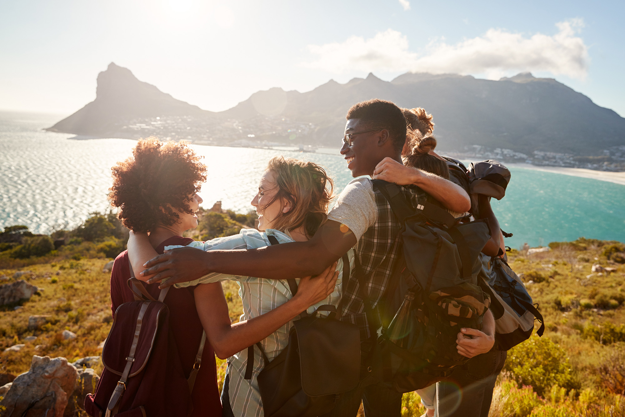 Five students in a huddle at the top of a cliff outlooking onto the sea.