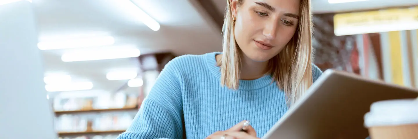 A student in the library checking work on a tablet.