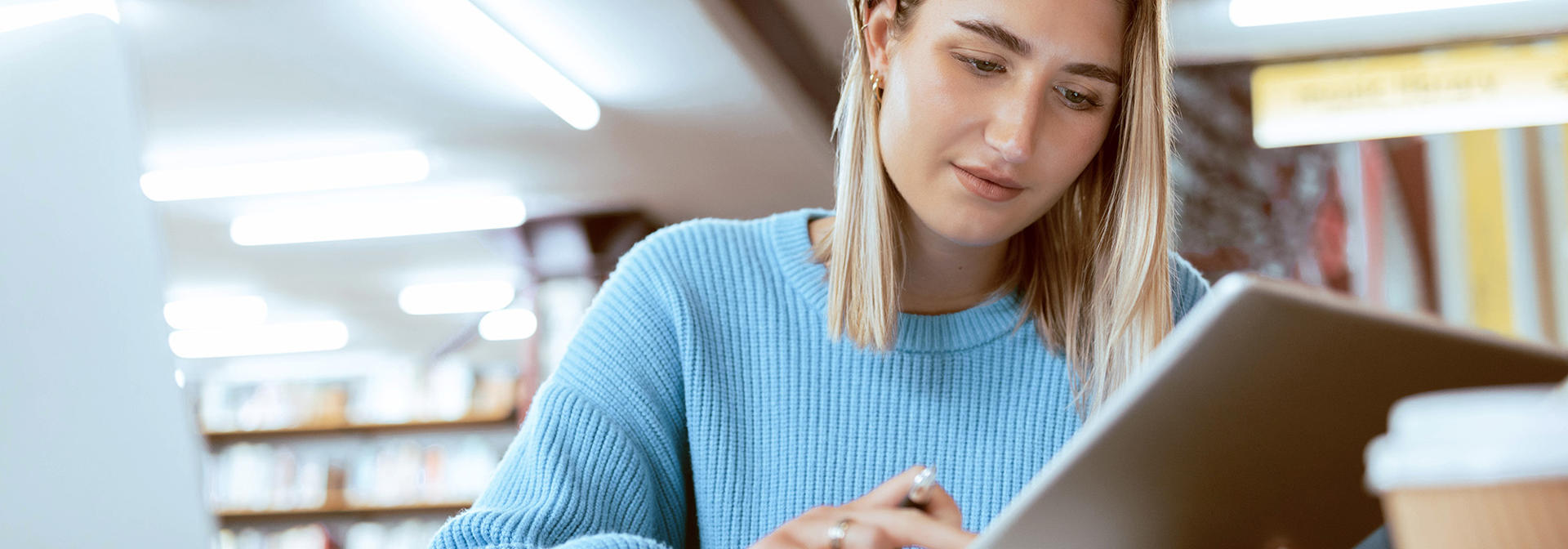 A student in the library checking work on a tablet.