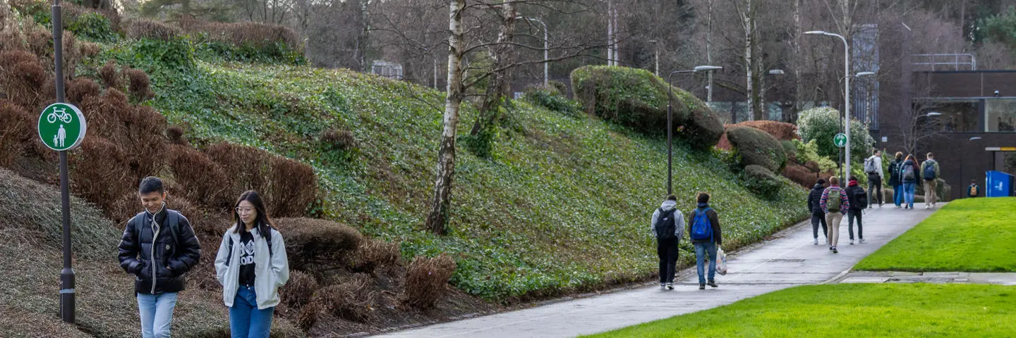 Two individuals walking along a path outside with grass and nature either side.