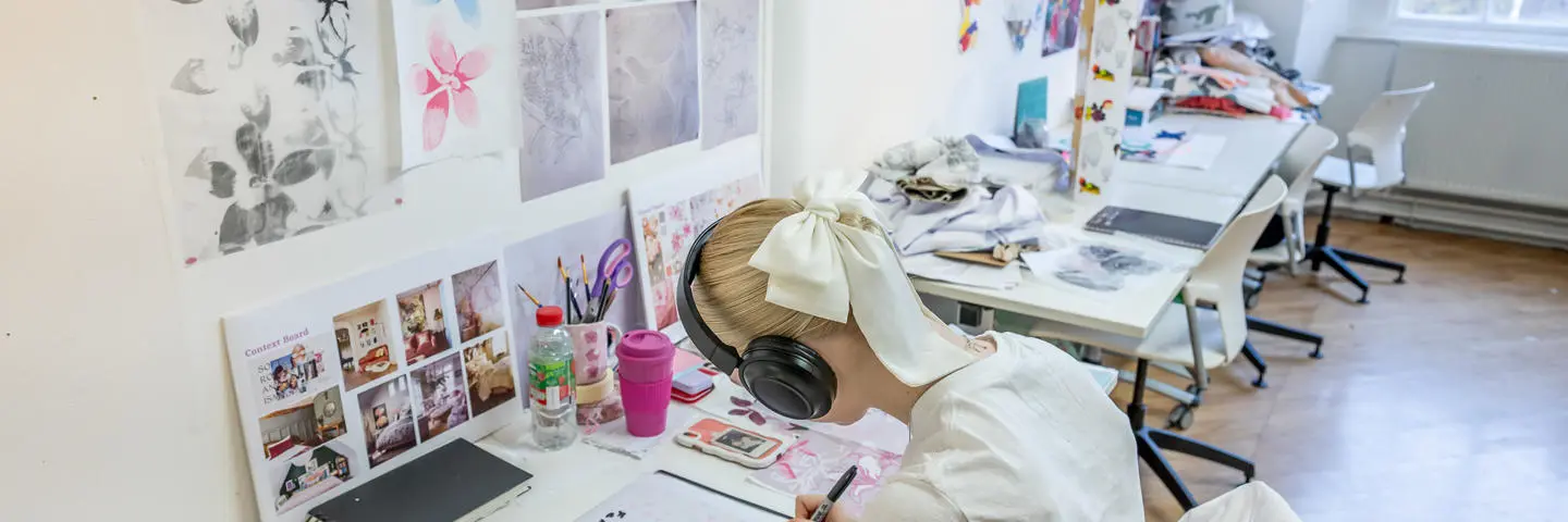 A design student leant over a desk drawing with a black pen.