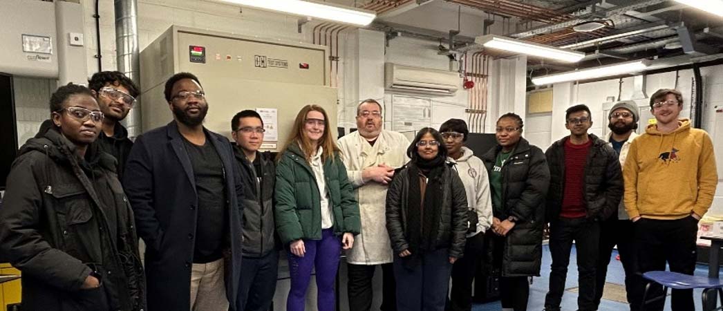 A diverse group of students standing in front of a large machine, looking at it with curiosity.