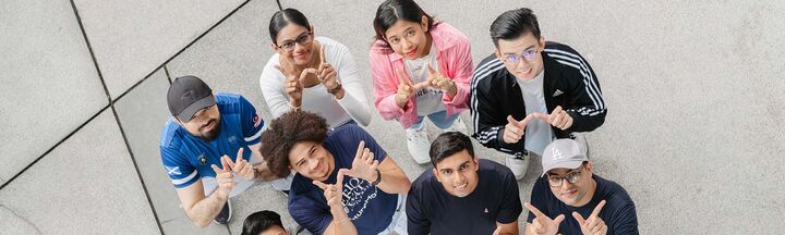 A group of students look up and make the 'w' sign with their hands 