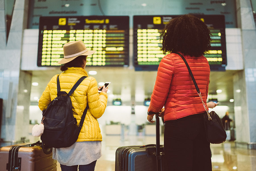 Two young female travellers look at an arrivals board in a terminal building