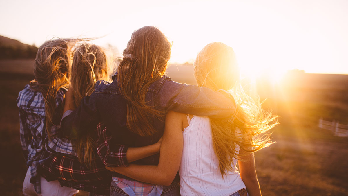 Group of young women with arms linked , standing in a field and looking towards the sunset